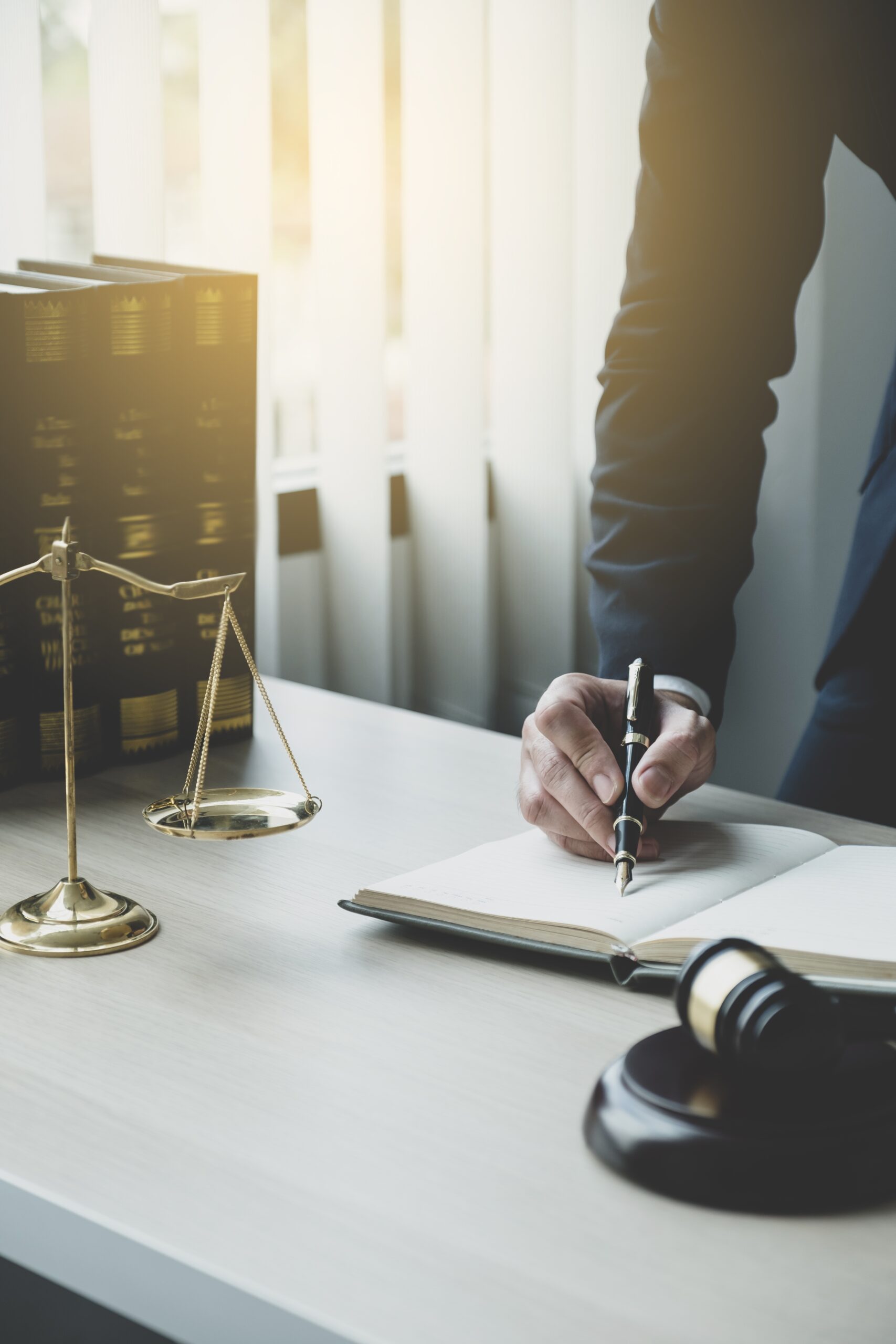 Lawyer hand holding pen and providing legal consult business dispute service at the office with justice scale and gavel hammer.